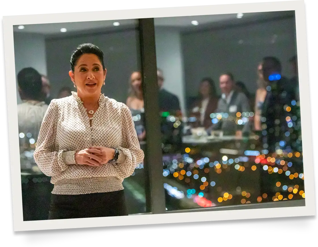 Susana Mendoza in a white shirt in front of a window in a high rise building talking to a group of people