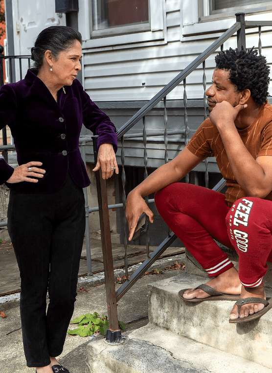 Susana Mendoza standing with her arm on a railing talking to a constituent sitting on the stairs next to her